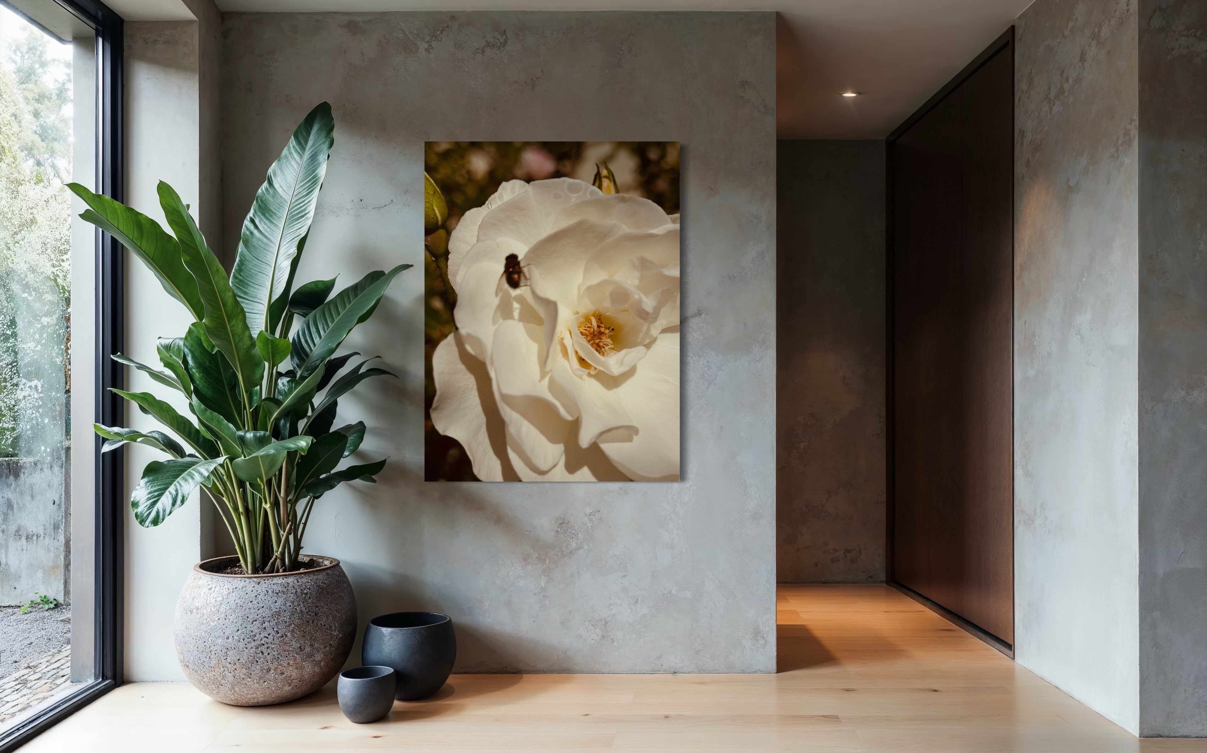 White rose artwork with a small fly hanging on a concrete wall beside a large indoor plant and ceramic vessels.